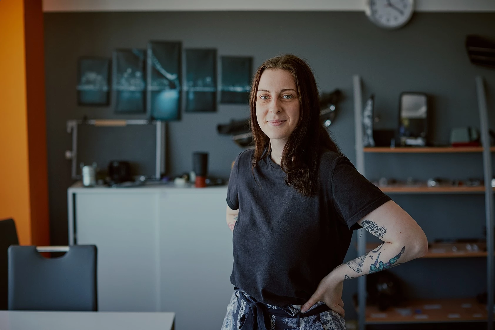 Young woman with tattoos smiling and standing confidently in a modern office environment."