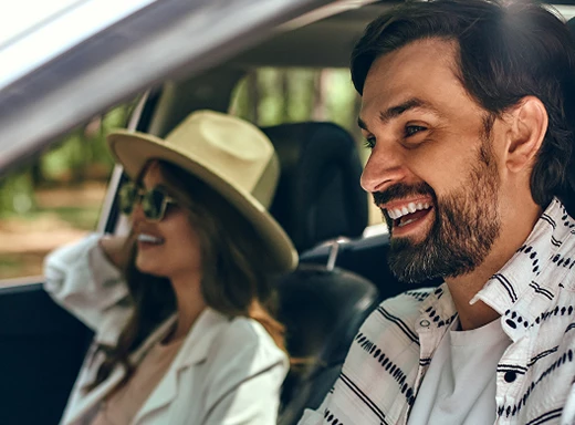 Smiling man driving a car with a woman passenger enjoying the ride.