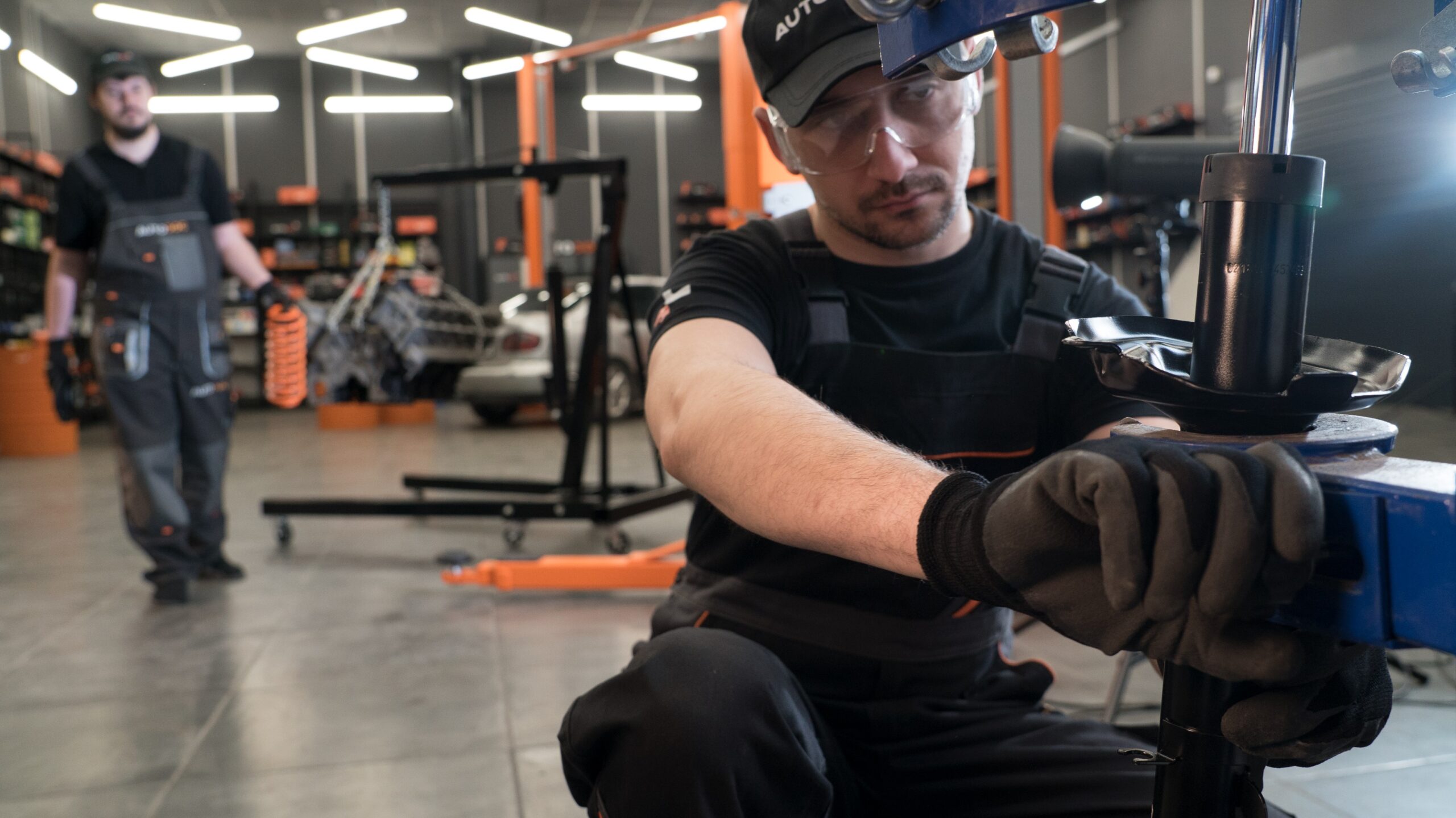 AUTODOC мechanic assembling a car shock absorber using a spring compressor in a modern auto repair workshop.